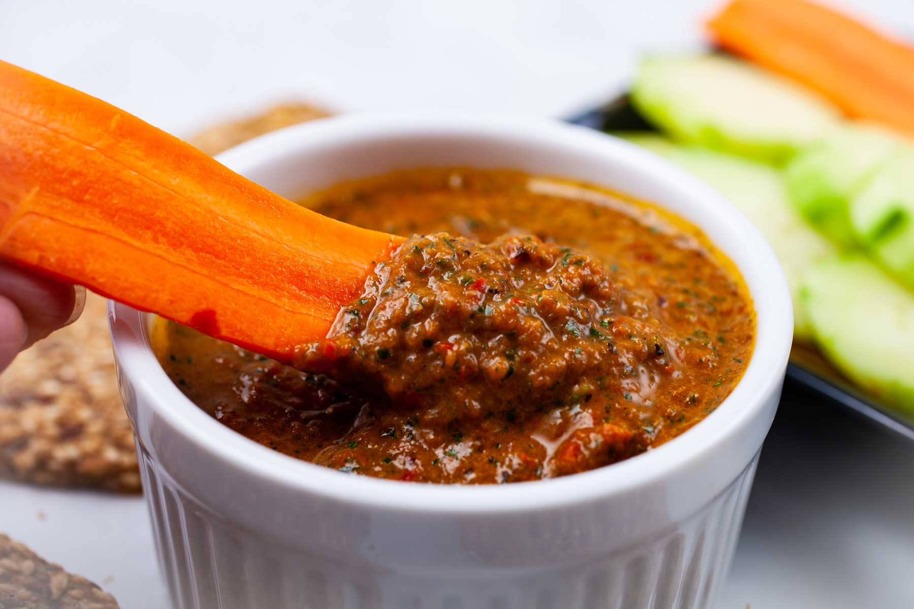 Someone dipping a sliced carrot in Italian red pepper dip.