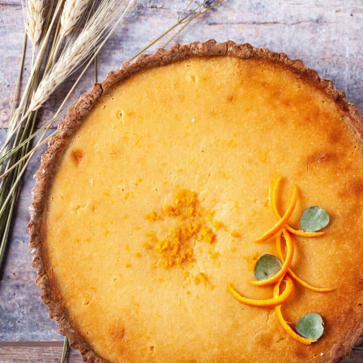 A beautiful golden cheese tart with orange peel decorations.
