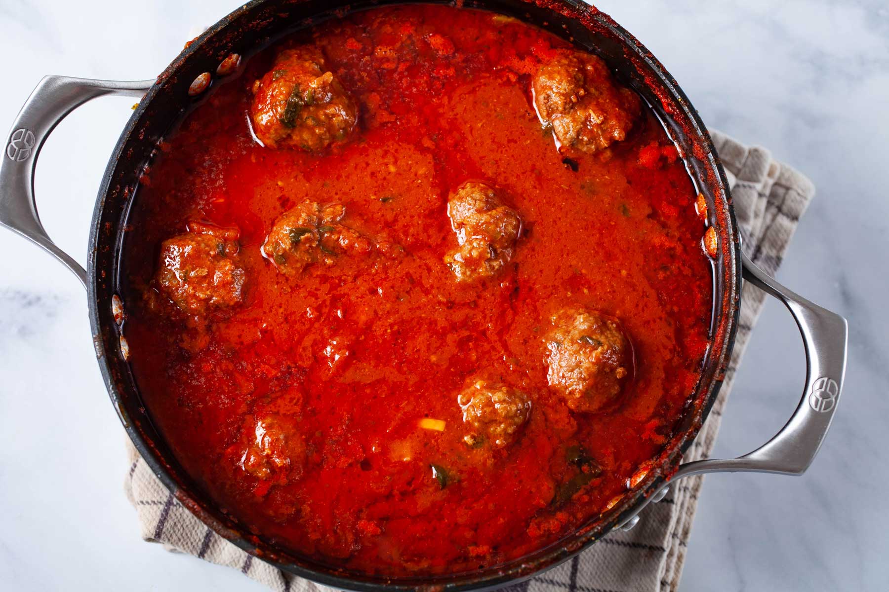 A large pot containing an Italian red sauce with beef meatballs.