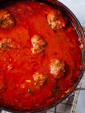 A large pot containing an Italian red sauce with beef meatballs.