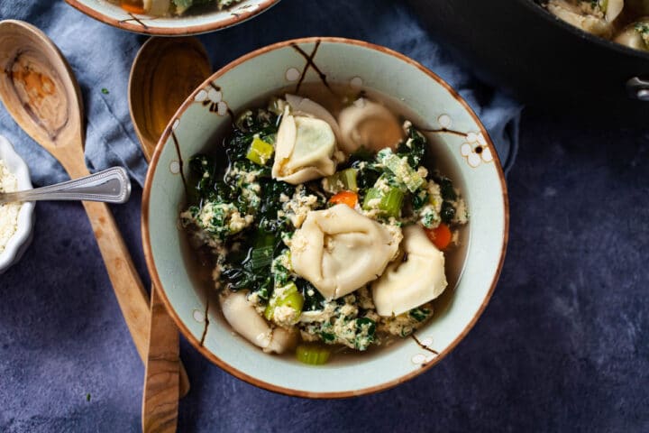 A bowl filled with Italian egg drop soup and vegetables with tortellini.