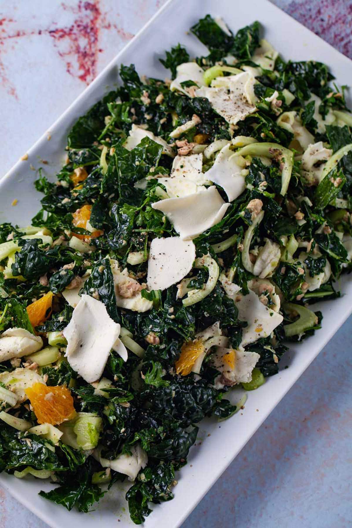 A large serving plate topped with a raw green kale and salmon salad with fennel, oranges, and mozzarella cheese.