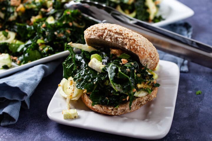 A seed bun generously filled with kale salmon salad served on a small plate.