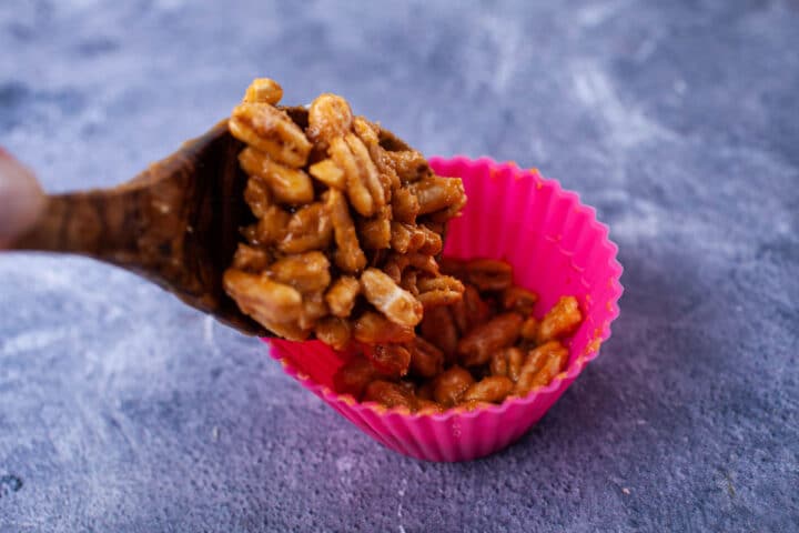 A spoon filling up a cupcake holder with sticky Kamut Puffs.