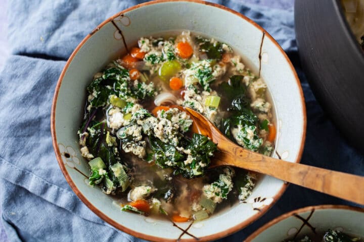 A wooden spoon resting in a bowl filled with Italian egg drop soup and vegetables.