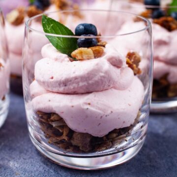 A single serve cheesecake in a cup topped with berries, mint leaves, and nut crumble.