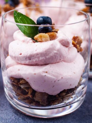 A single serve cheesecake in a cup topped with berries, mint leaves, and nut crumble.