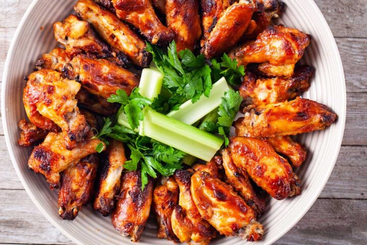 A large round plate filled with golden baked chicken wings plus some thighs, garnished with fresh celery sticks and parsley.