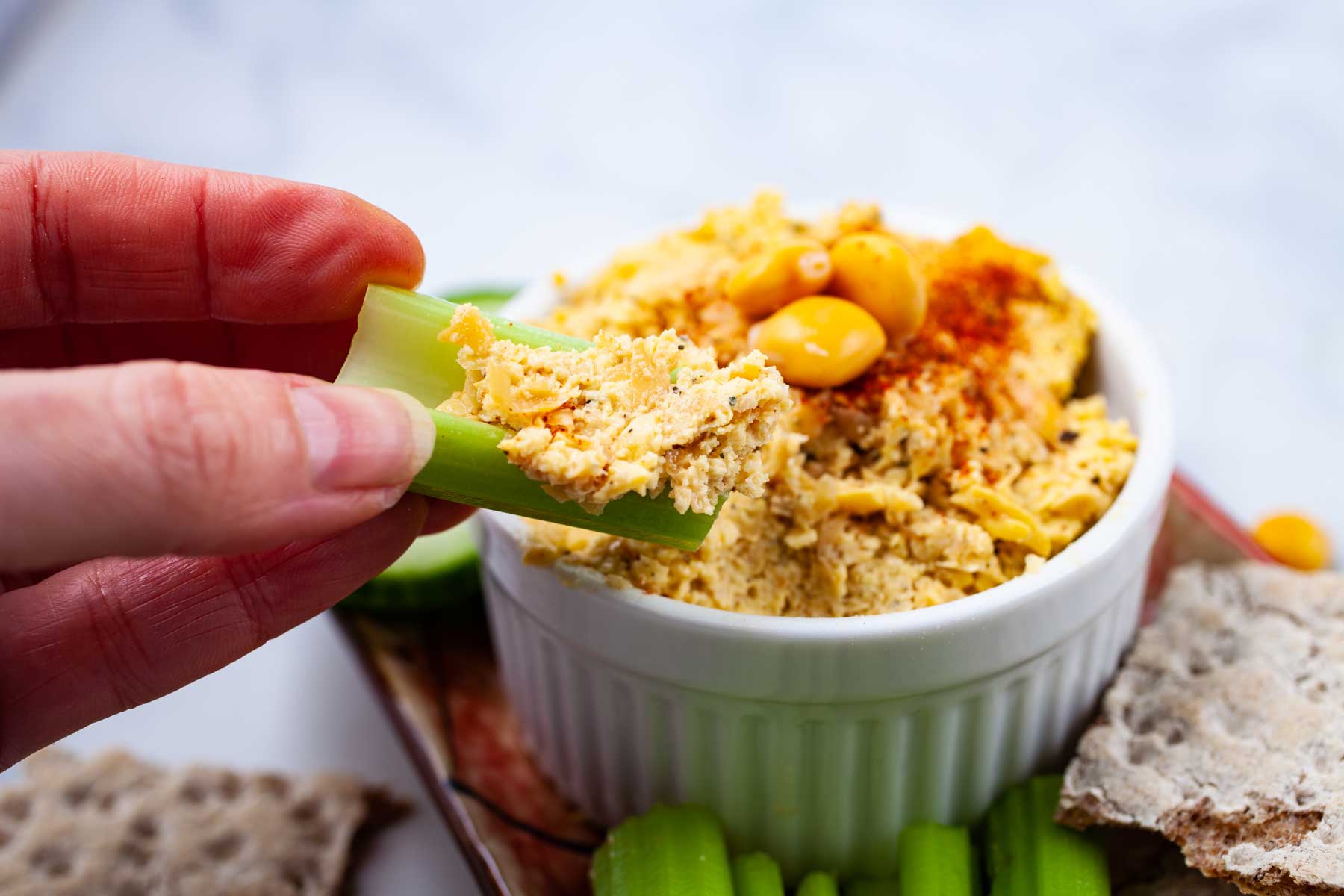 A hand holding a piece of celery topped with lupin bean hummus.