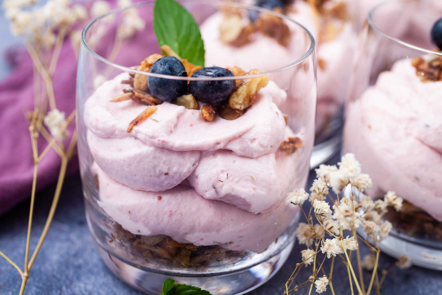 A single serve cheesecake in a cup topped with berries, mint leaves, and nut crumble.