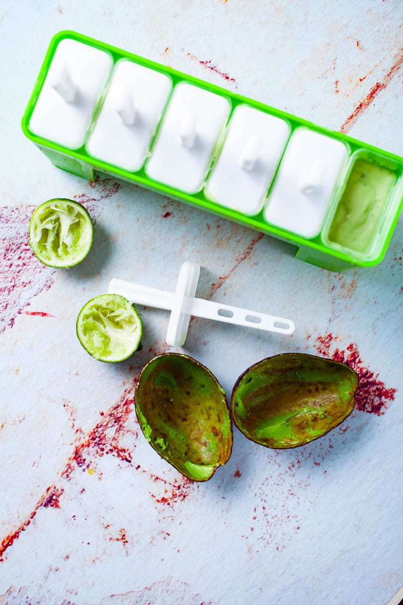 Ice pop molds filled with a green avocado-lime puree and surrounded by avocado and lime peel.