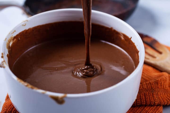 Creamy chocolate nut butter dripping into a large bowl containing more of that nut butter.