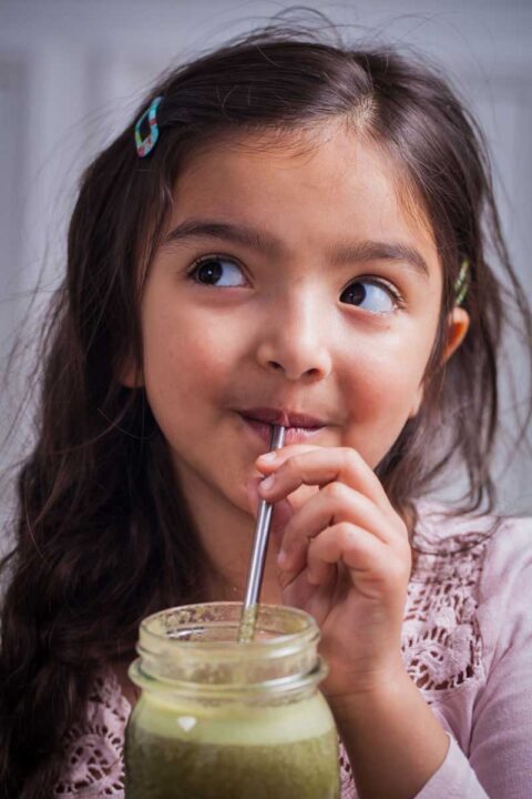 A smiling girl drinking a smoothie from a stainless steel straw.