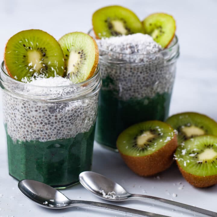 Two jars filled with chia pudding, infused with a kiwi sauce, topped with coconut shreds, and slices of fresh kiwi.