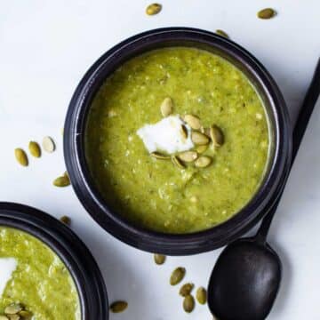 Avocado leek soup served in small bowls topped with seeds and coconut cream.
