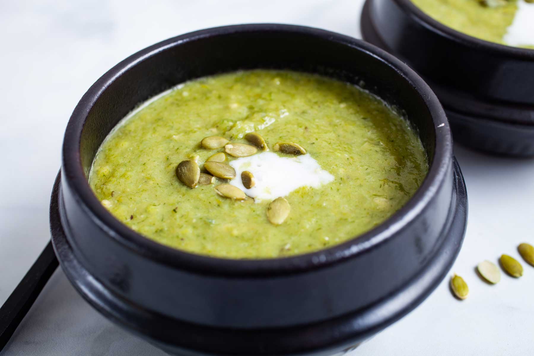 Avocado leek soup served in small bowls topped with seeds and coconut cream.
