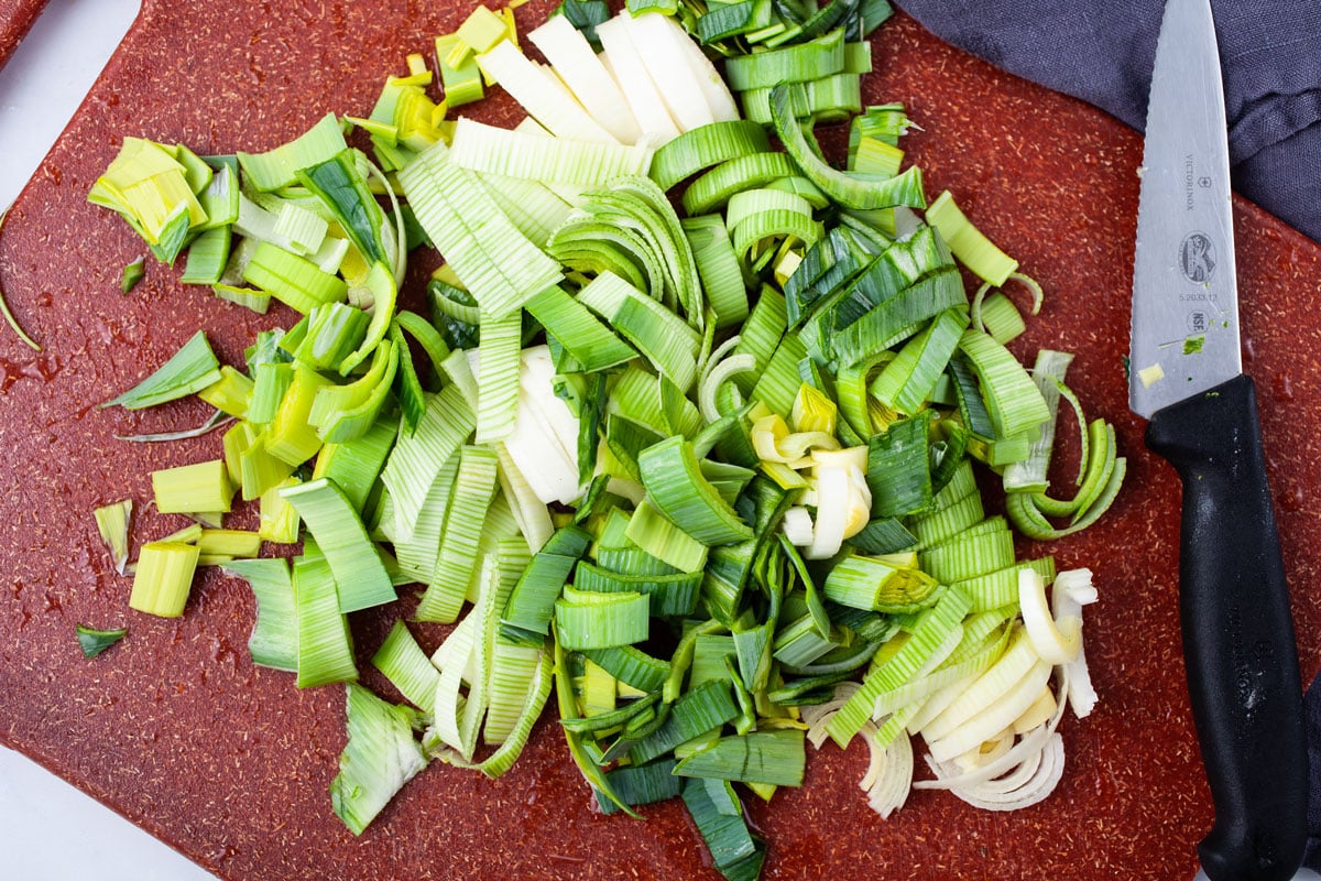 Chopped leek on a cutting board next to a large kitchen knife.