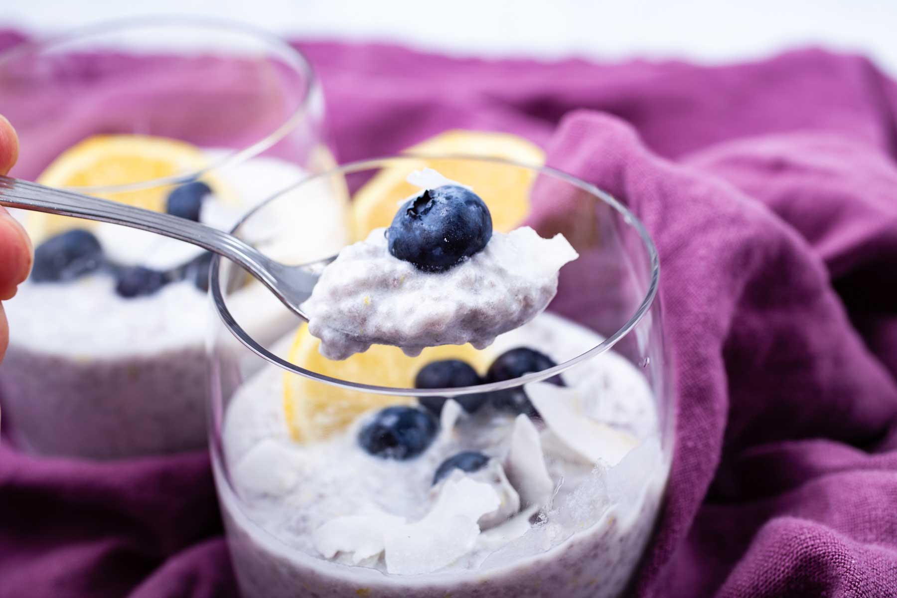 A hand holding a full spoon of lemon chia pudding over a cup.