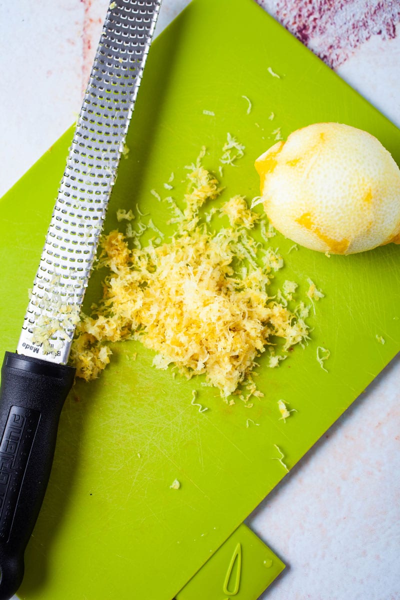 A grated lemon with zest peel and the grater next to it on a cutting board.