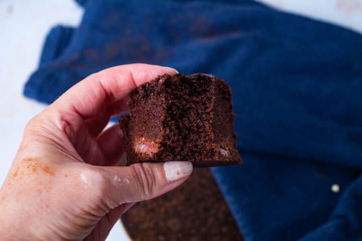 A hand holding a piece of bitten chocolate cake.