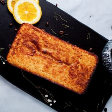 An orange low carb cake beautifully displayed on a wooden board with a cup of coffee.