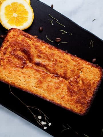 An orange low carb cake beautifully displayed on a wooden board with a cup of coffee.