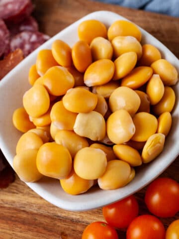 A close-up of a small bowl with prepared Lupini beans displayed on a charcuterie board.