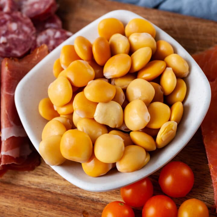 A close-up of a small bowl with prepared Lupini beans displayed on a charcuterie board.