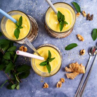 Three glasses filled with mango lassi, topped with mint leaves and each carrying a straw.