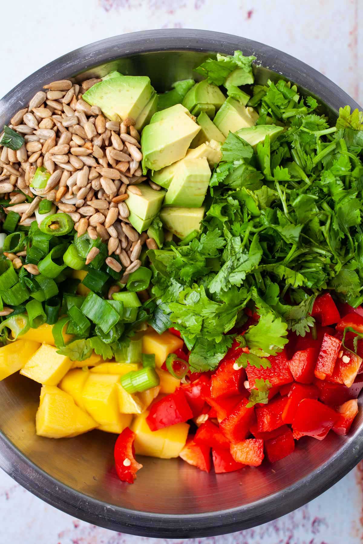 Chopped bell pepper, avocado, cilantro, onions, mango, and sunflower seeds in a large bowl.