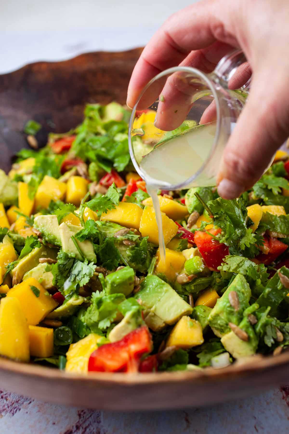 Someone pouring a lime dressing over a mango and avocado salad.