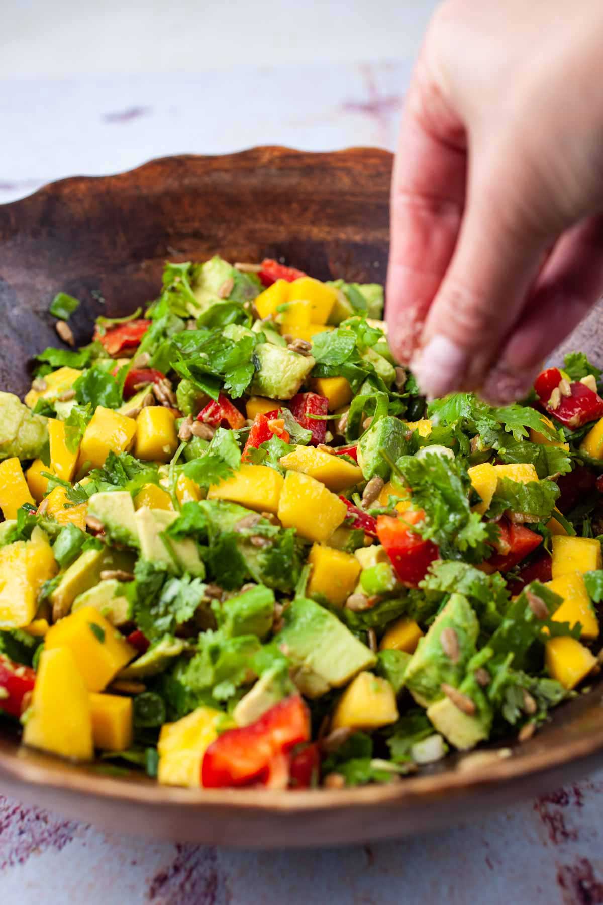 Someone seasoning a mango avocado salad.