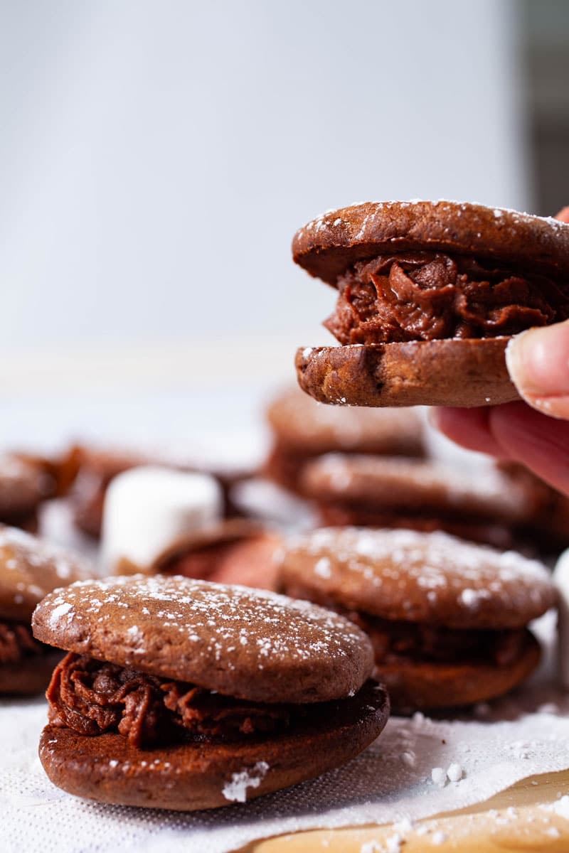 A close-up of a hand holding a mascarpone filled sandwich cookie.