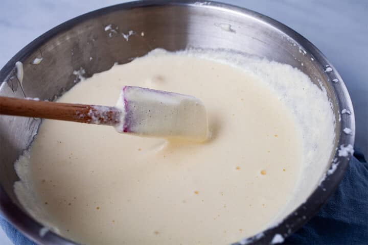 A spatula folding in egg white into wet ingredients in a stainless steel bowl.