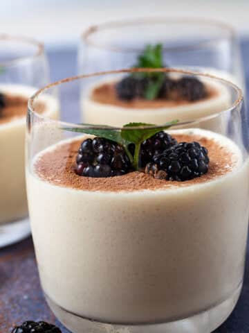 Glasses filled with mascarpone mousse, types with cacao powder and garnished with blackberries and mint leaves.