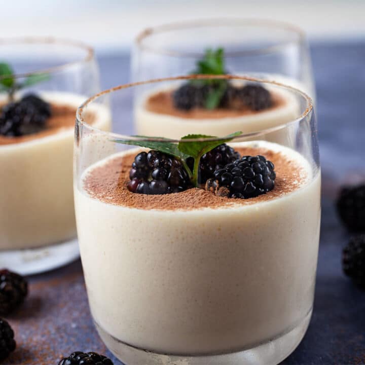Glasses filled with mascarpone mousse, types with cacao powder and garnished with blackberries and mint leaves.