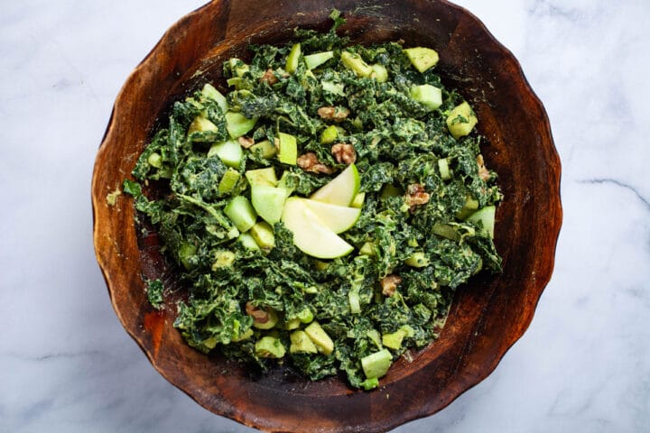 A wooden bowl filled with a creamy apple kale salad.