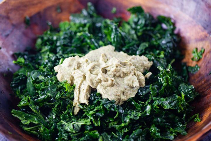 Green chopped kale with a dollop of avocado pesto in a large wooden salad bowl.