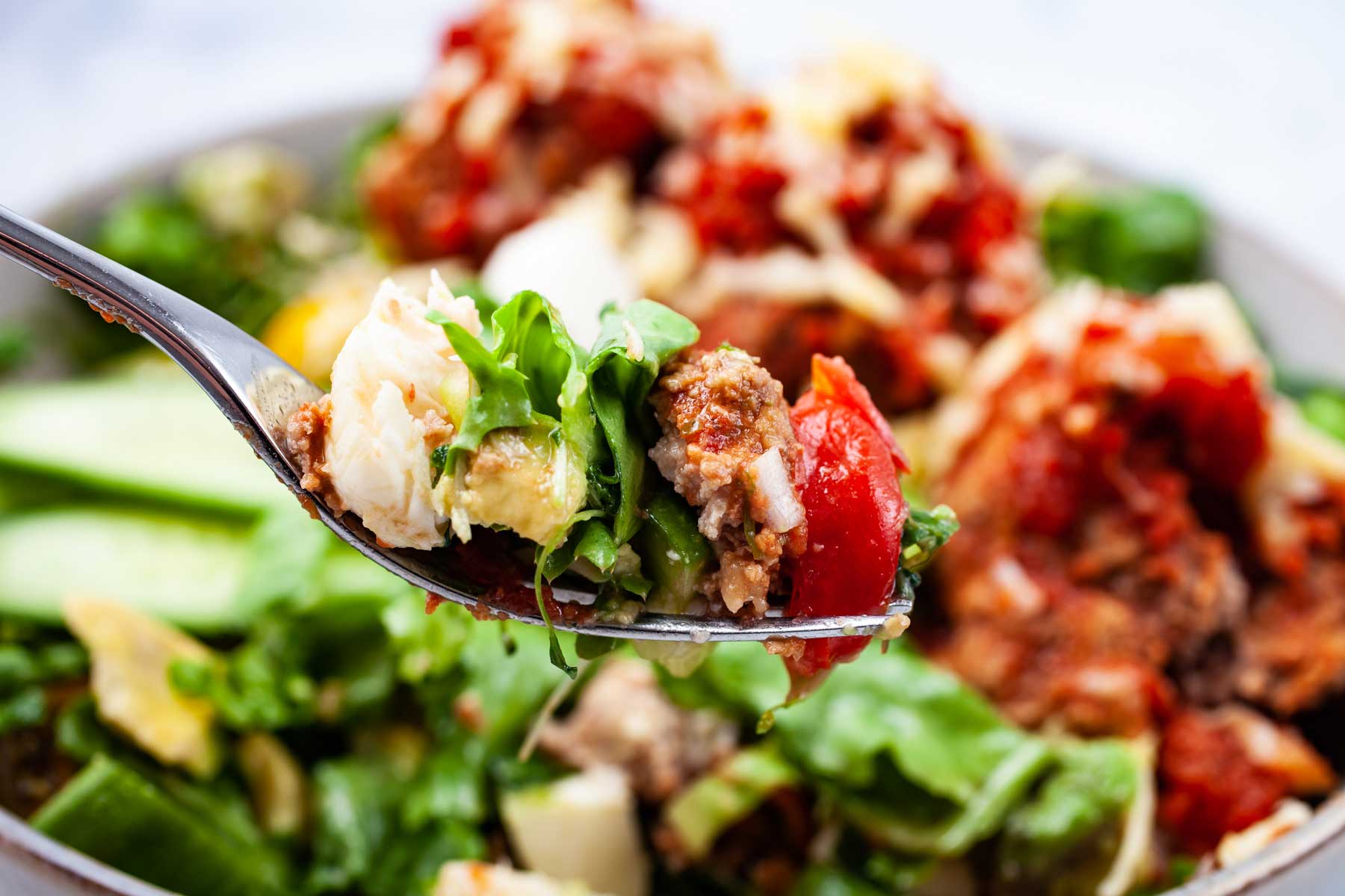 A fork taking a bite our of an Italian meatball salad bowl.