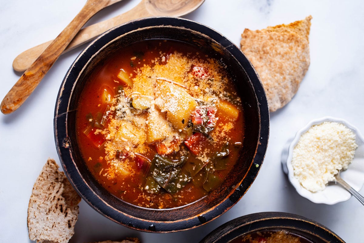 A tomato based vegetable soup with potatoes served in a wooden bowl and topped with grated Parmesan cheese.