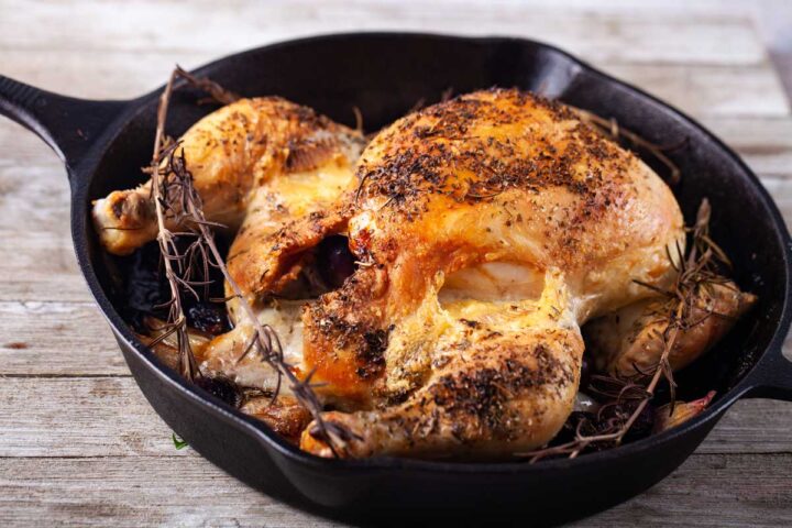 Whole roasted chicken in an iron skillet filled with brie, grapes and seasoned with rosemary.
