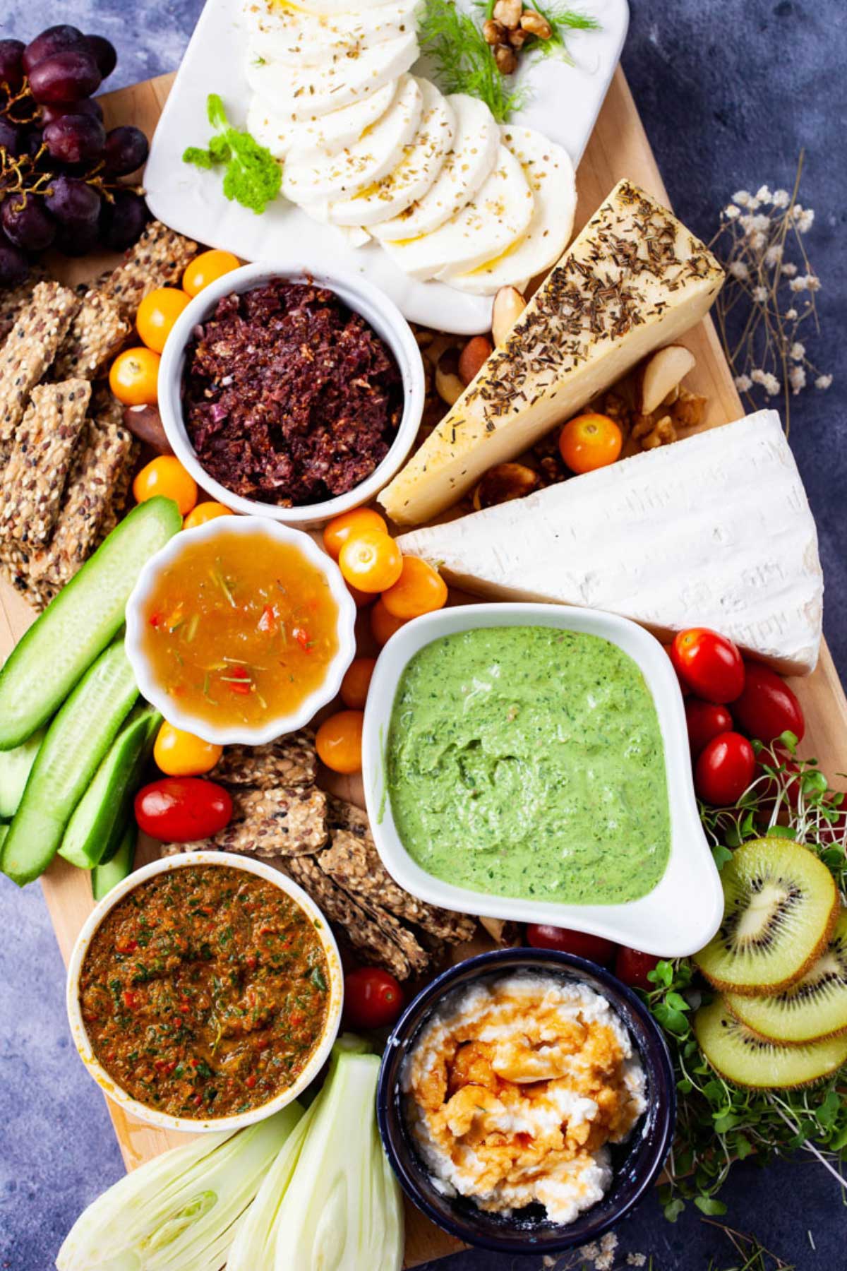 An assortment of cheeses, bruschetta, veggies, dried and fresh fruits, and toppings displayed on a board.