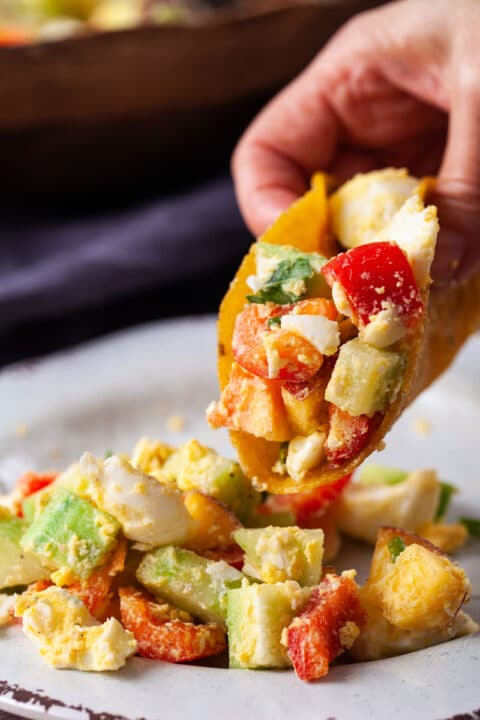 A hand holding a taco filled with Mediterranean egg salad.