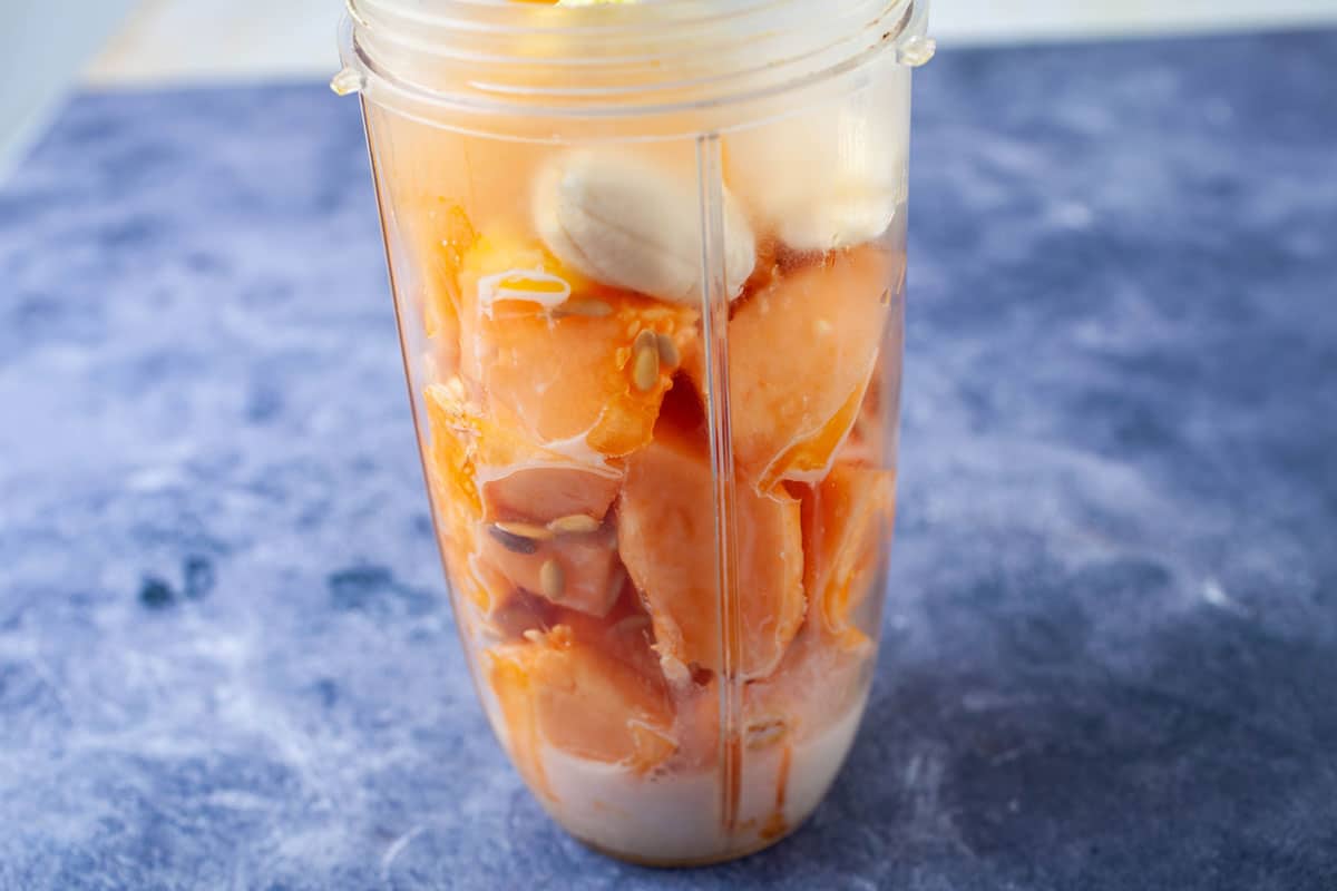 A blender filled with cantaloupe pieces, banana, and plant milk.