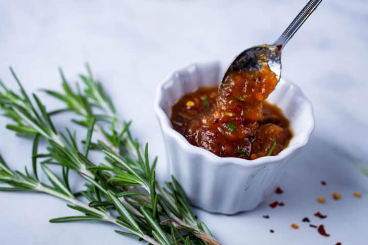 A spoon taking a bit of spiced jam out of a ramekin bowl.