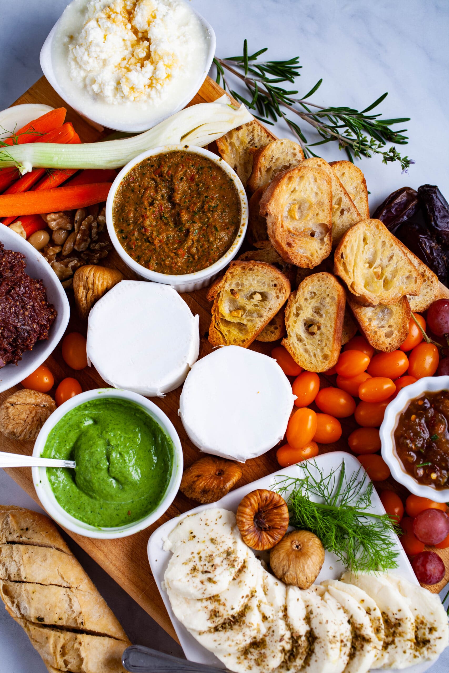 An assortment of cheeses, bruschetta, veggies, dried and fresh fruits, and toppings displayed on a board.