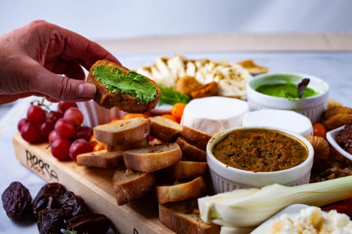 A hand holding a bruschetta topped with a green topping over a mezzo board.