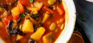 Two rustic looking bowls filled with vegetable minestrone soup and served with two wooden spoons.