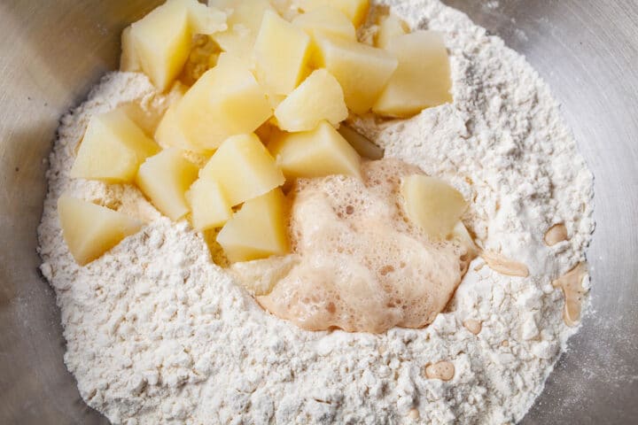 A bowl with flour and topped with leavened yeast and cooked potatoes.