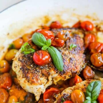 Baked chicken topped with mini tomatoes and basil leaves.